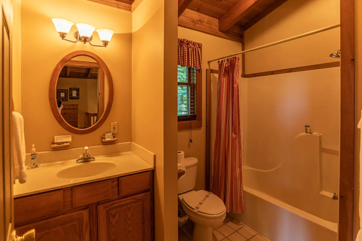 A bathroom with a round mirror above wooden cabinetry, a shower area, and a window with curtains. The space is bright, functional, and inviting—perfect for morning routines or unwinding after a day outdoors.