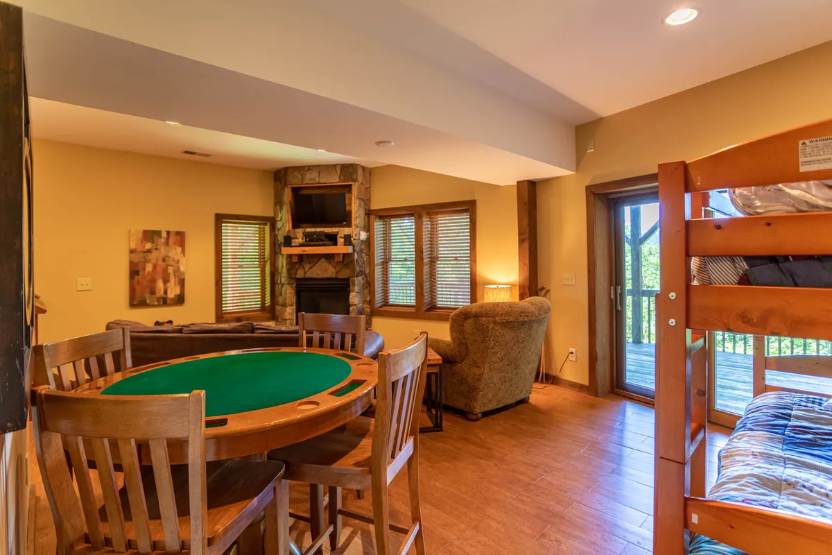 A friendly recreation space showcasing a dining table with a poker table design, a comfortable armchair, large windows providing natural light, and bunk beds. The layout makes it ideal for game nights, casual meals, and family relaxation, with a sense of openness and adaptability.