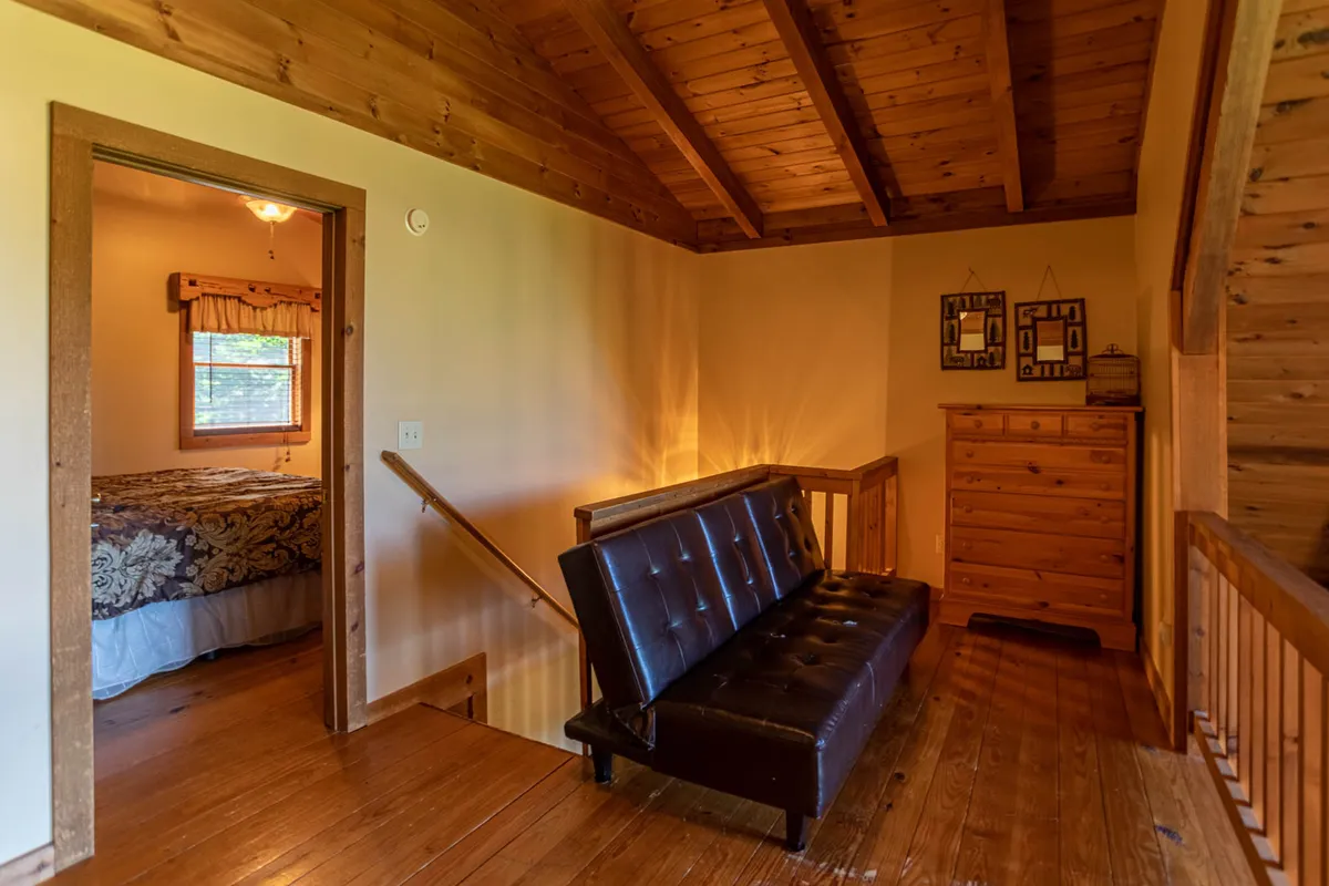 A cozy space with a sofa, wooden furniture, a decorative mirror, and a partial view into a bedroom. The setting is intimate, ideal for reading, relaxing, or quiet moments alone or together.