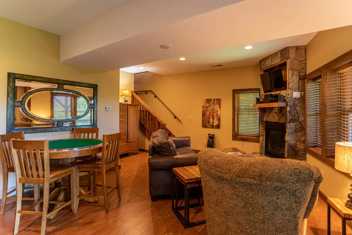 A cozy, multi-functional living space featuring a comfortable seating area by a crackling fireplace, a dining table perfect for group activities, and a staircase hinting at the home's multi-level layout. The warm, relaxed atmosphere is ideal for both lively family games and intimate fireside conversations.
