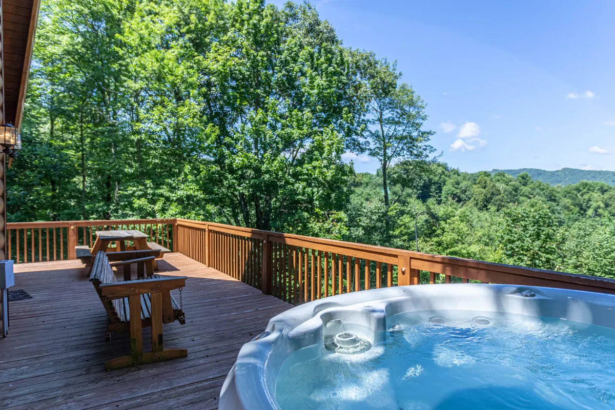 A relaxing deck scene featuring a bubbling hot tub and comfortable seating, all set against a backdrop of lush greenery. The deck offers sweeping views into the surrounding nature, embodying the sense of peace and scenic beauty that guests can enjoy after a day of mountain exploration.