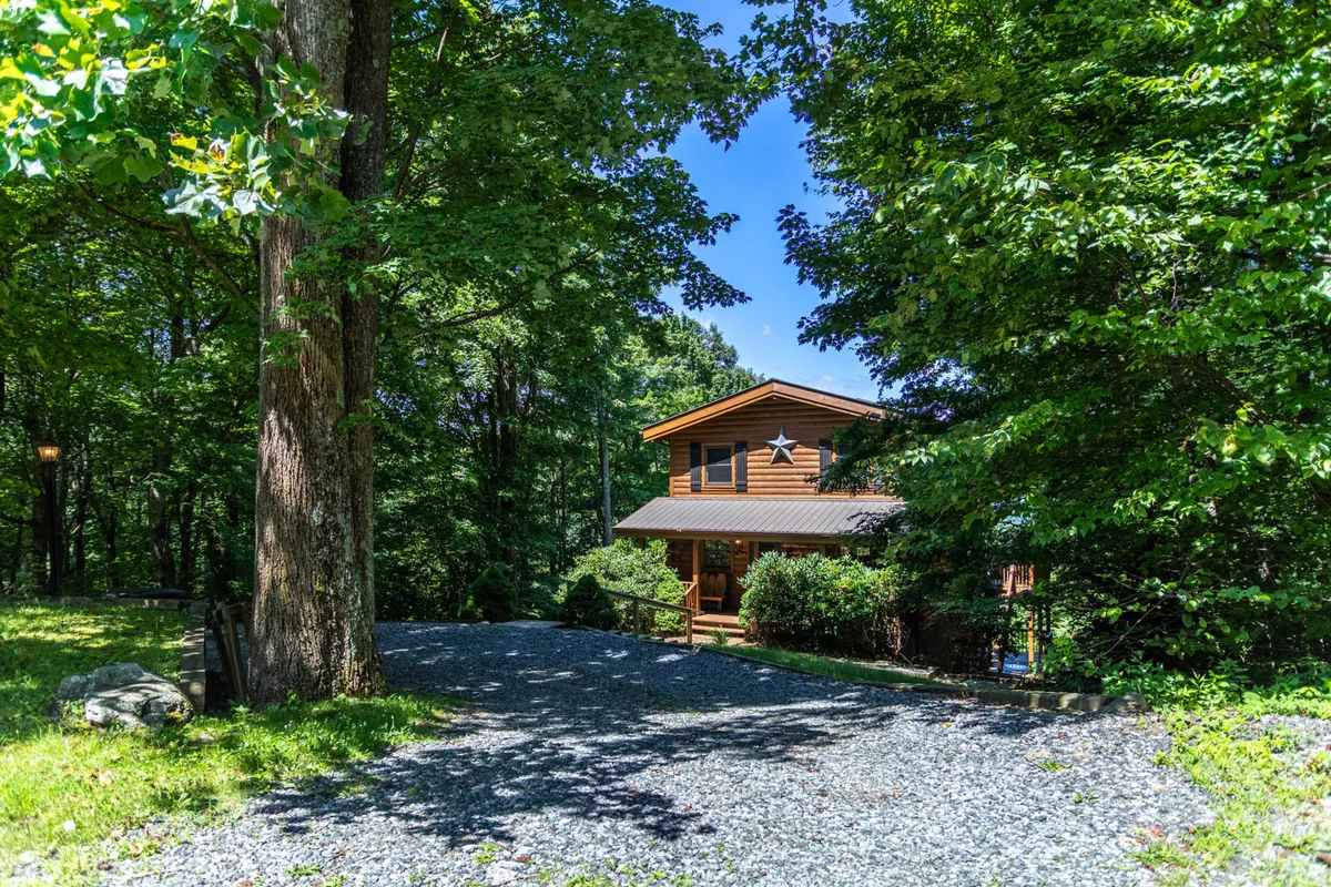 A tranquil exterior shot of the house surrounded by large, mature trees and a gravel driveway. The scene features an inviting yard perfect for outdoor gatherings, nature walks, and enjoying the mountain air. The home stands as a welcoming base for adventure, set against the lush backdrop of the High Country.